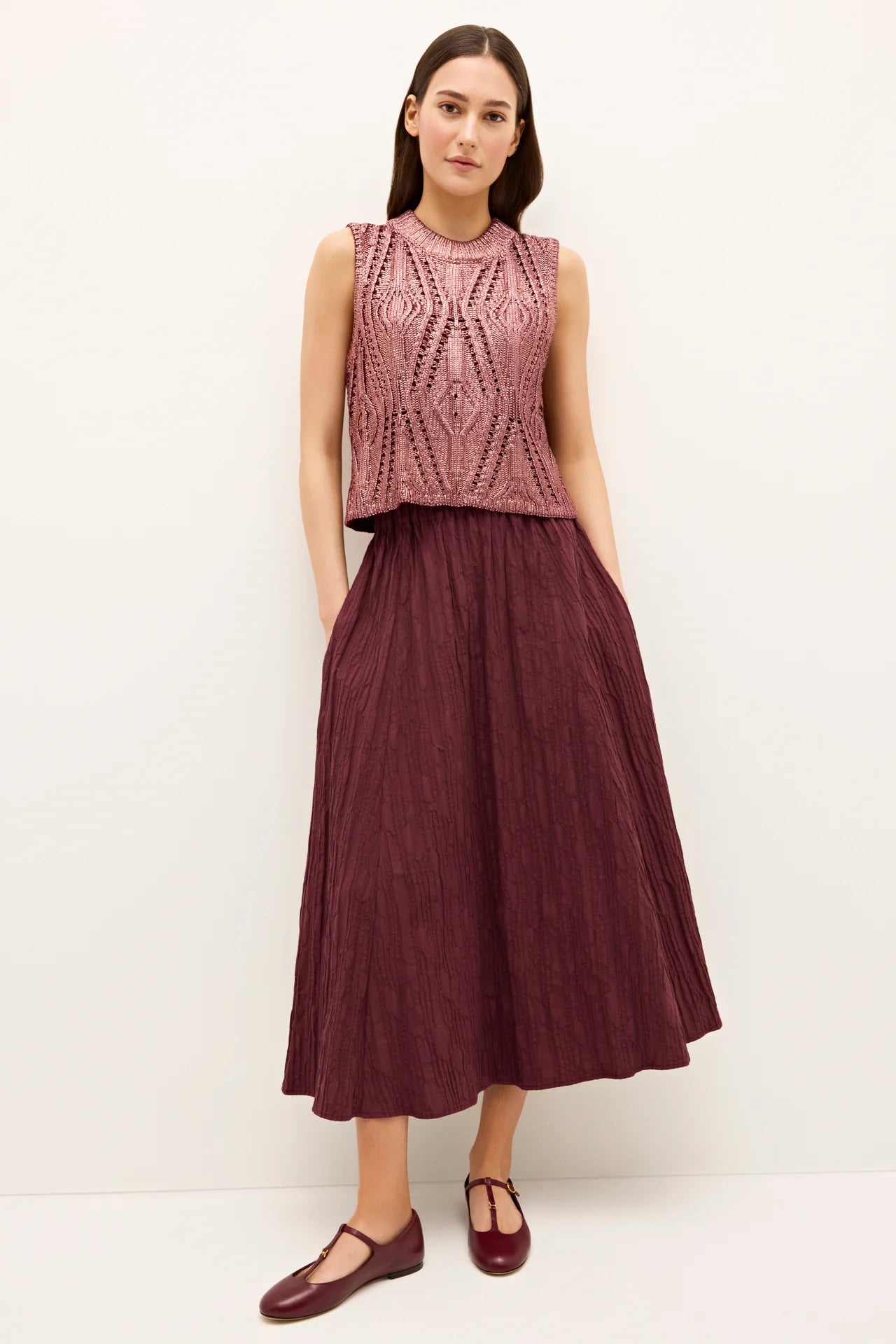 Woman wearing a pink sleeveless top and maroon skirt on a white background.