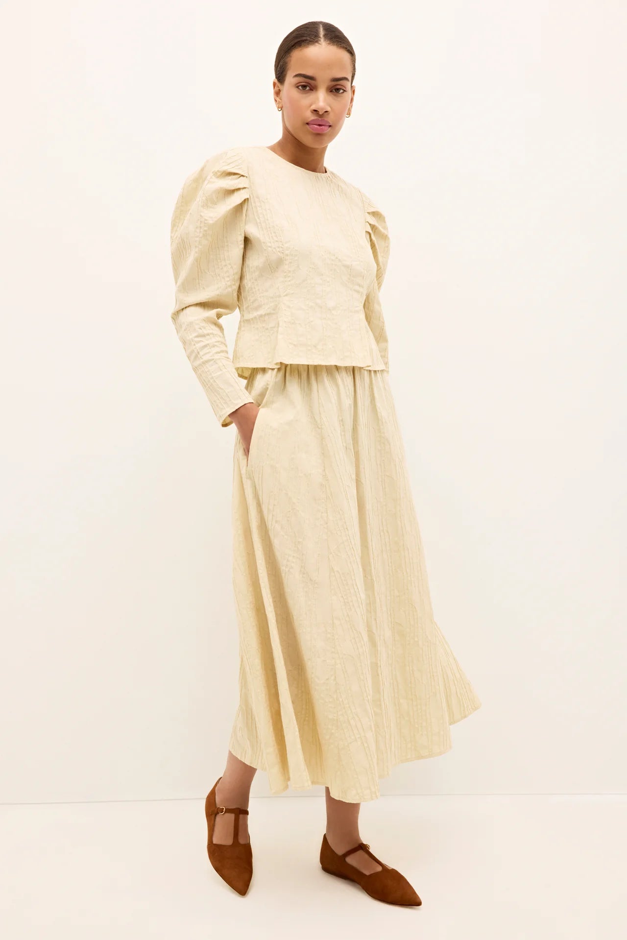 Woman wearing a cream outfit with a top and skirt on a white background.