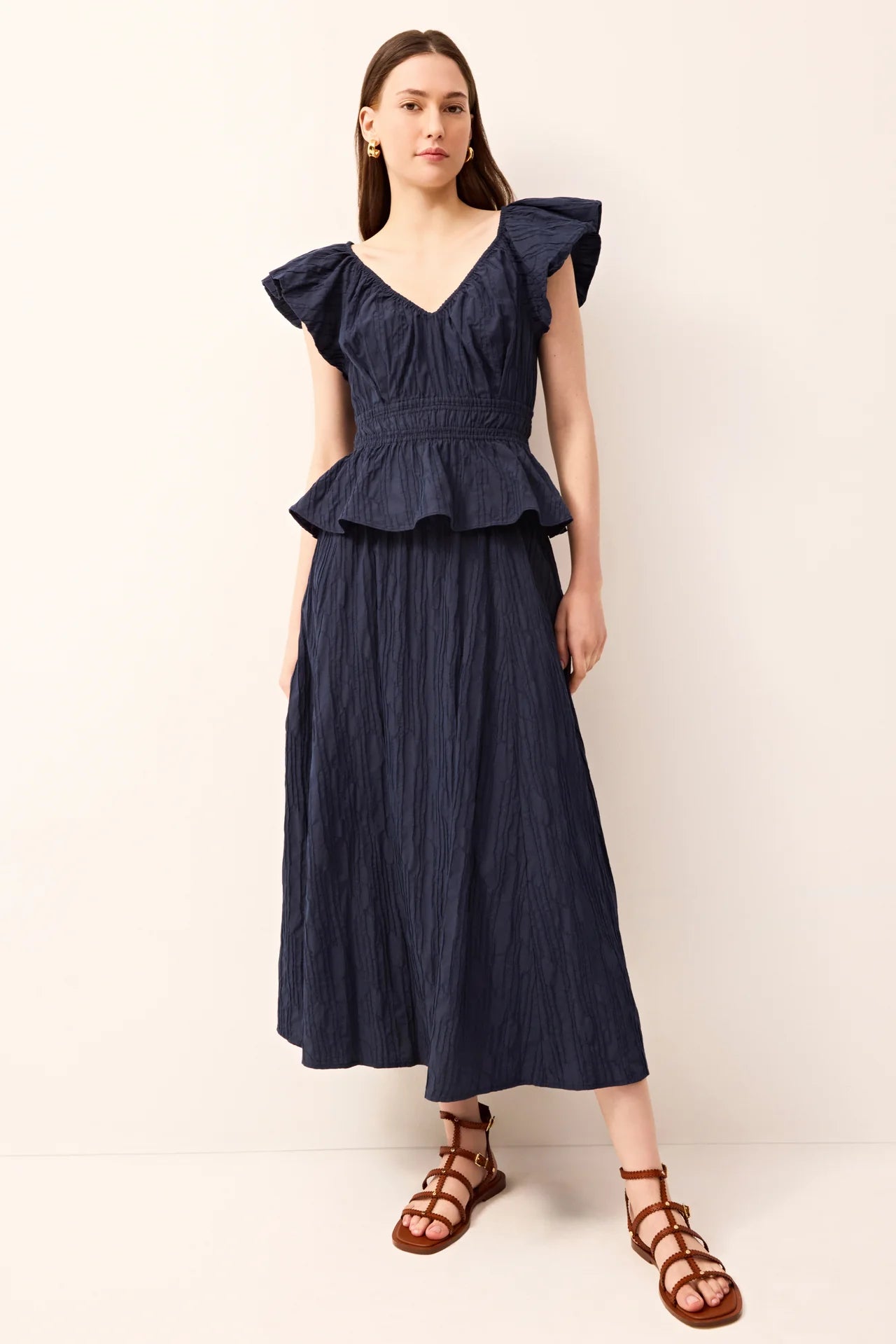 Woman wearing a navy blue dress with ruffled sleeves against a white background.