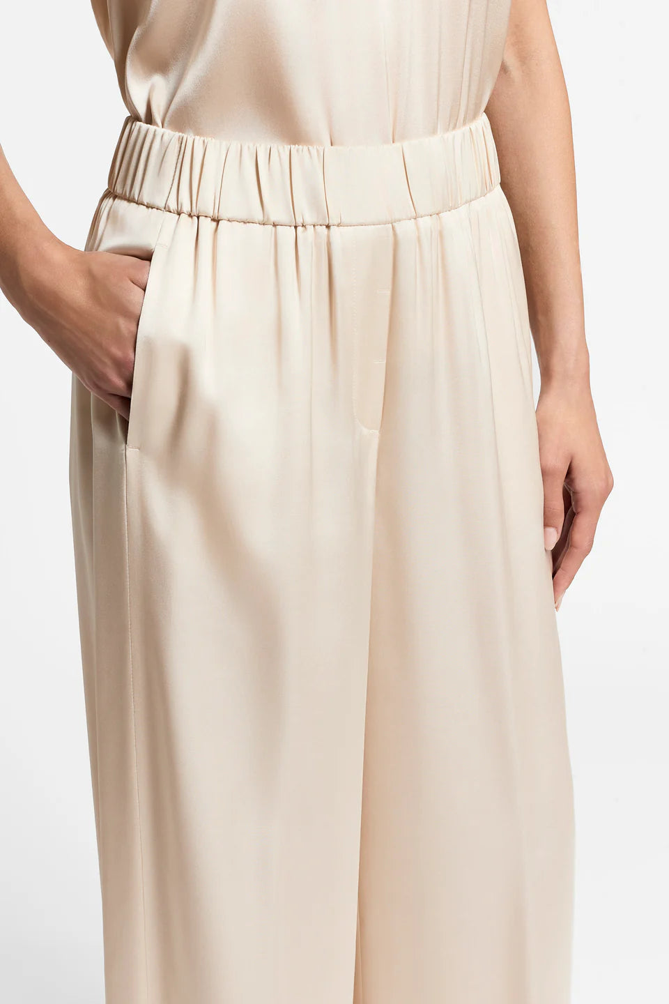 Close-up of a woman wearing beige satin trousers on a plain background.