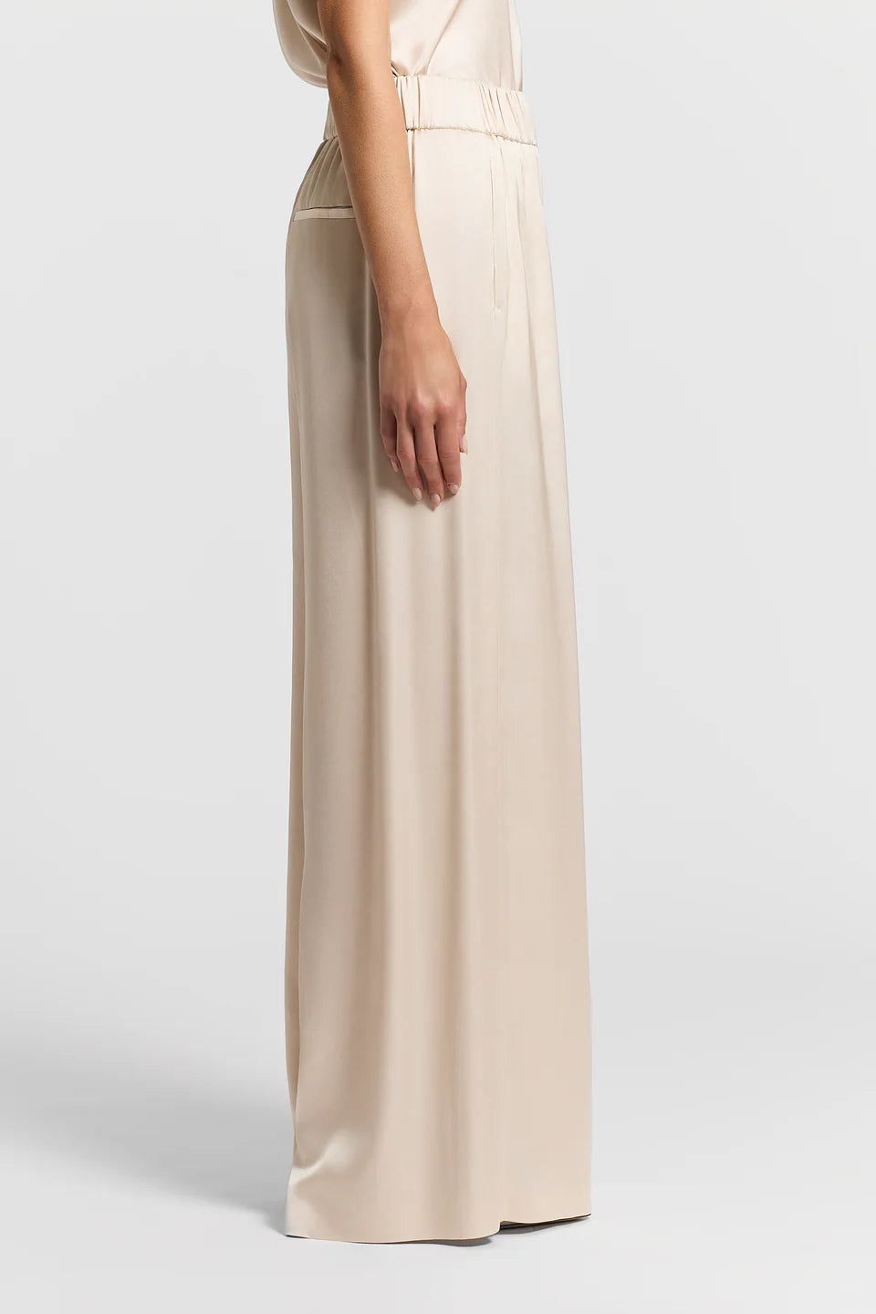 Side view of a woman wearing beige wide-leg satin pants on a white background.