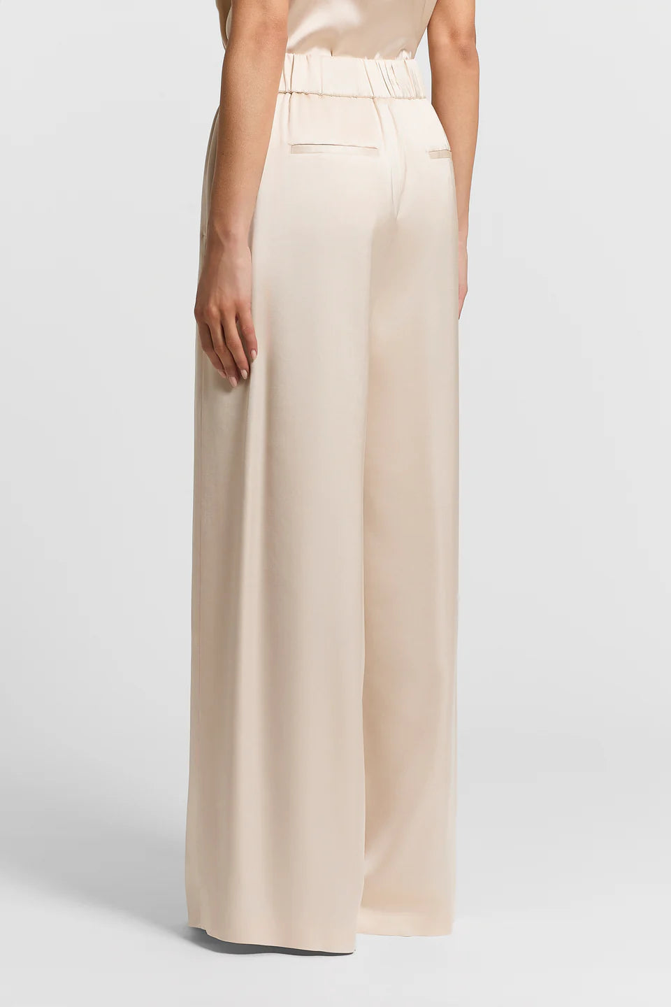 Back view of a woman wearing beige wide-leg satin pants on a white background.