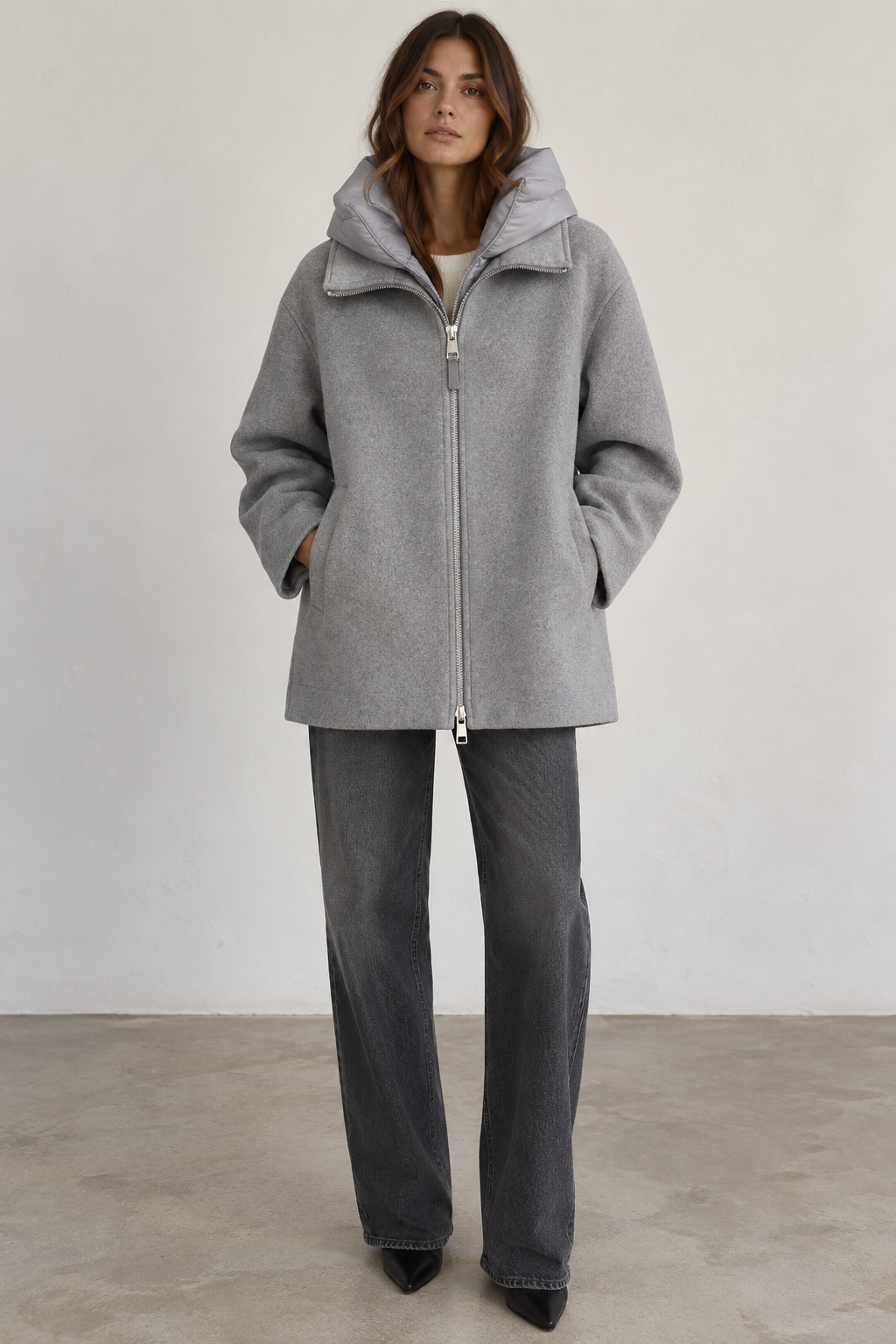 Model wearing a Seventy gray wool-blend coat with a removable padded collar, relaxed silhouette, silver front zipper, and side pockets, styled with charcoal wide-leg jeans and black pointed-toe boots.