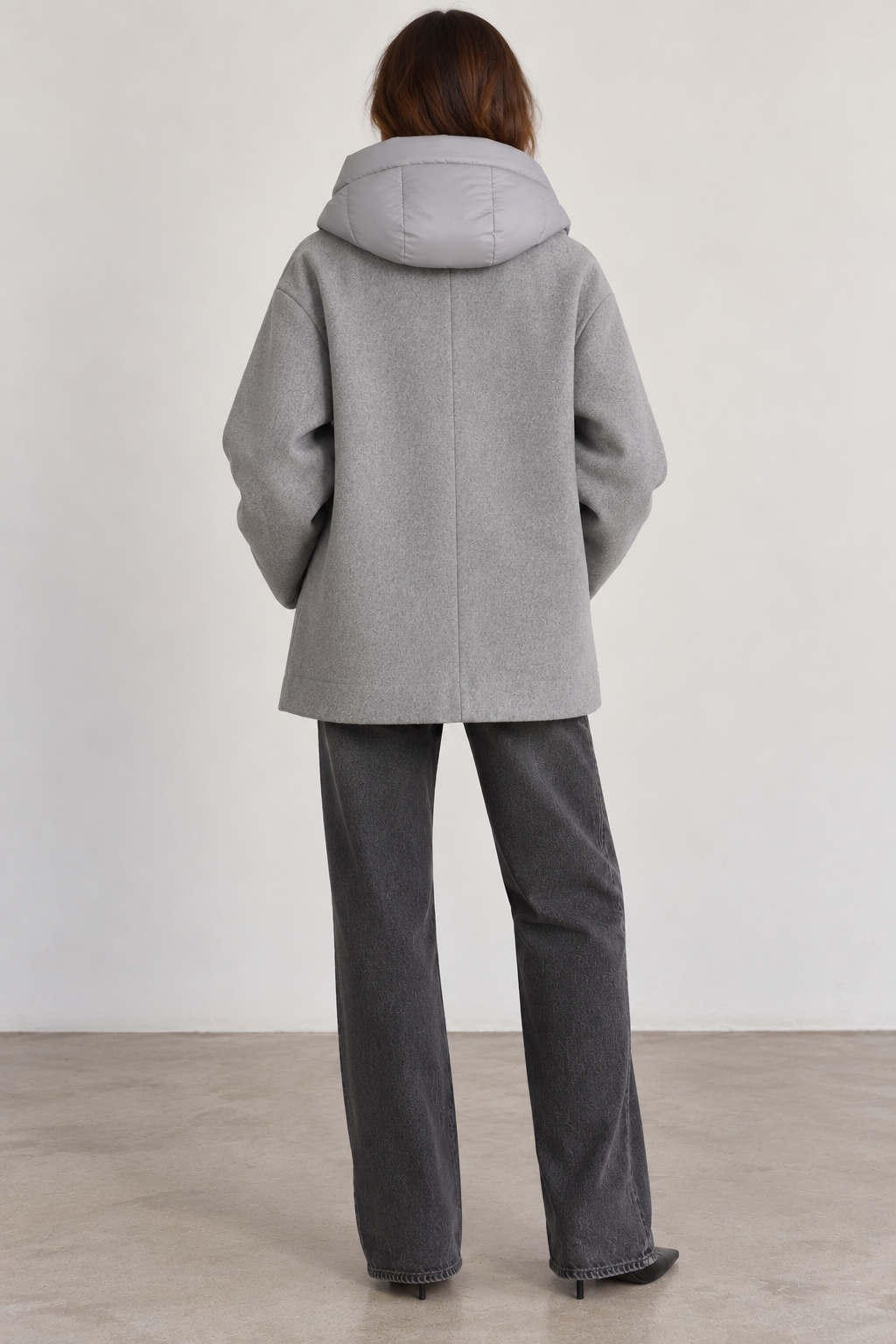 Back view of model wearing a Seventy gray wool-blend coat featuring a relaxed, boxy silhouette, removable padded gray hood, long sleeves, and a straight hem, styled with charcoal wide-leg jeans and black pointed-toe boots.