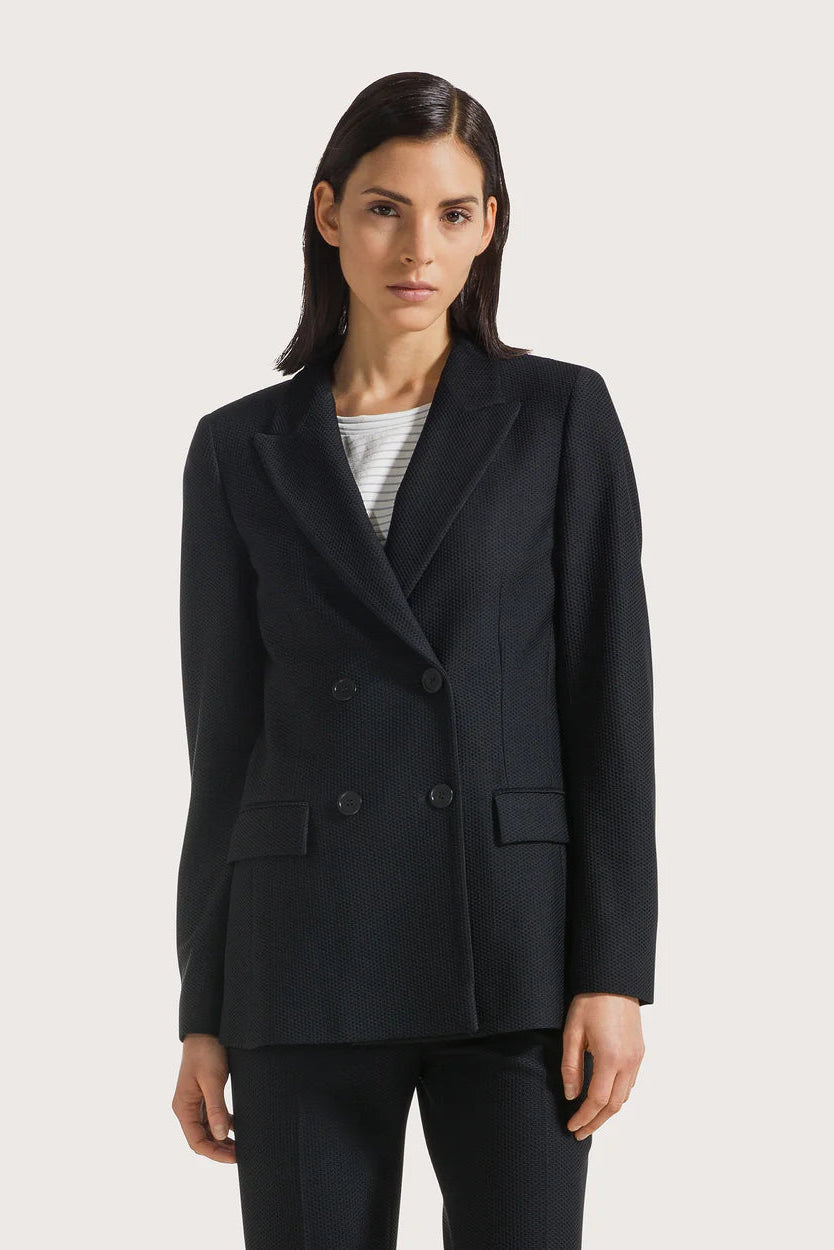 Woman wearing a black blazer over a striped shirt on a white background.