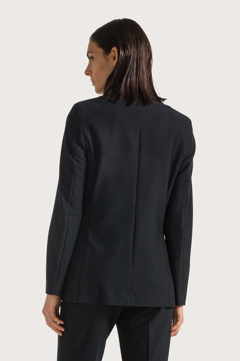 The back of a woman wearing a black blazer from the back on a light gray background.