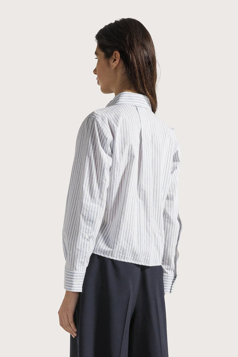 The back of a woman wearing a white and blue striped shirt with a plain background.