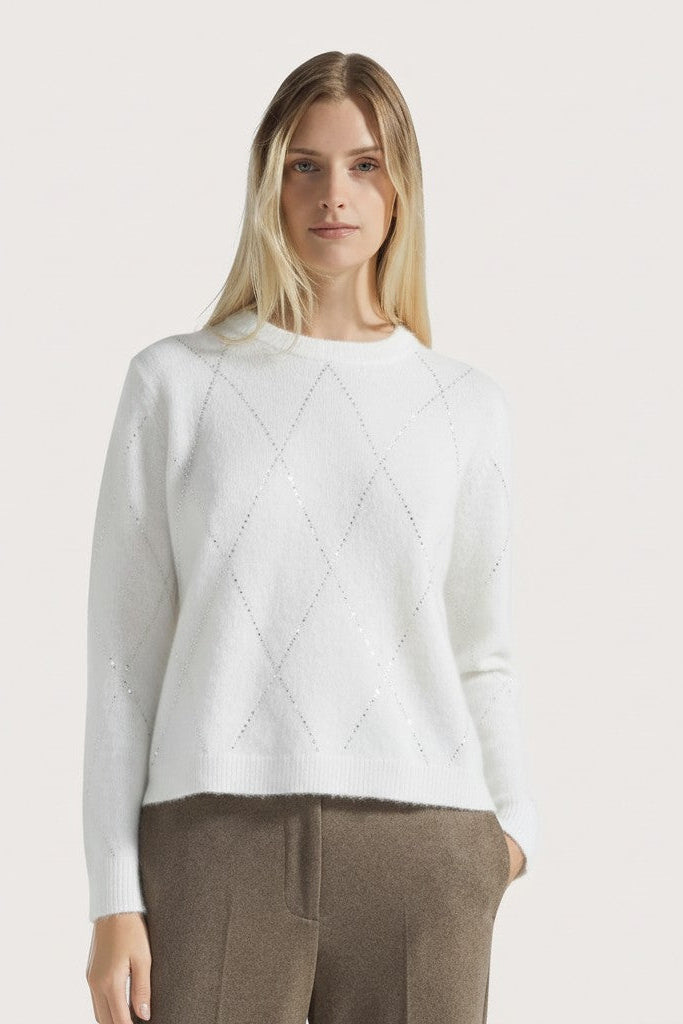 Woman wearing a white sweater with a diamond pattern on a light gray background.