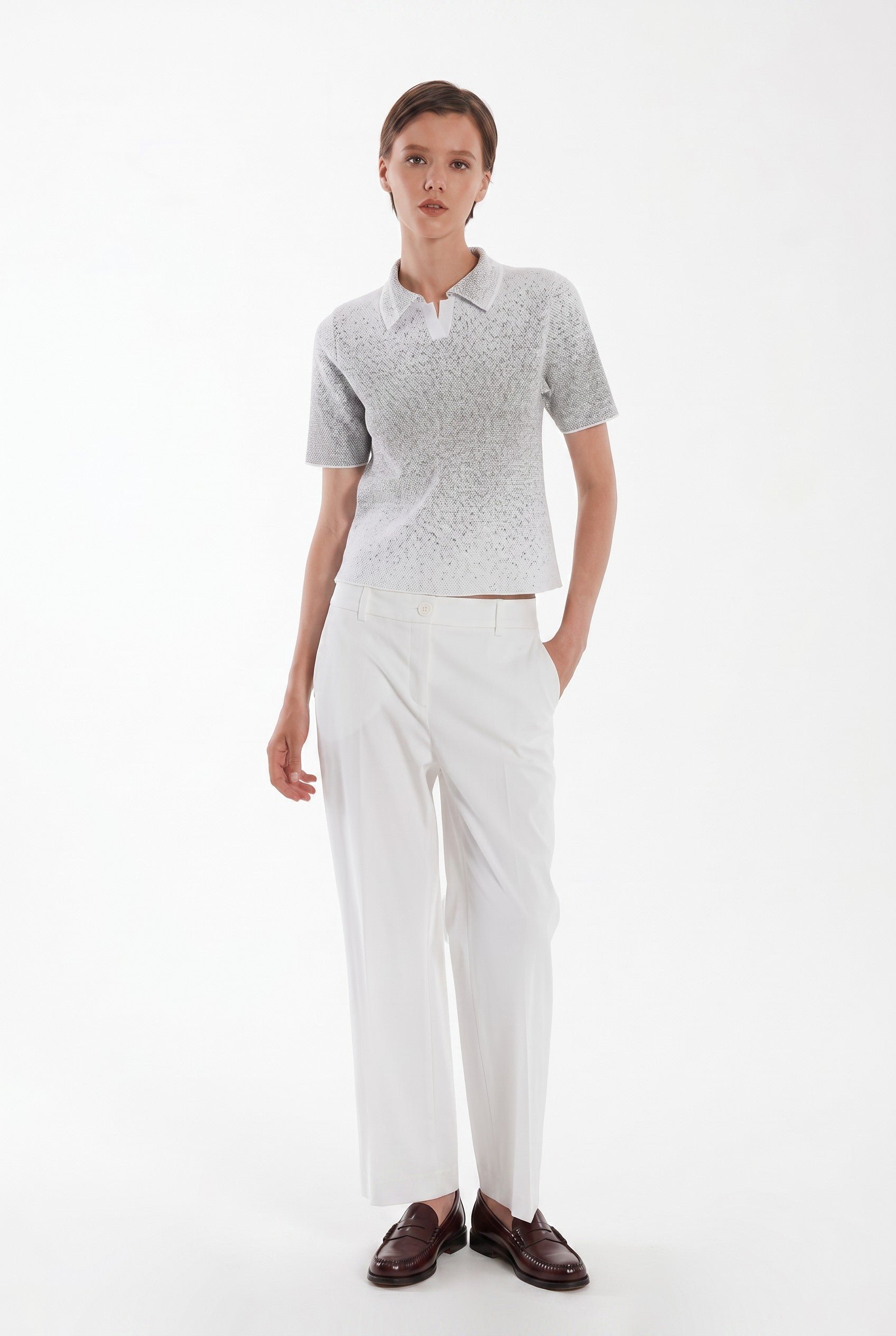 Woman wearing a gray polo shirt and white pants on a white background.
