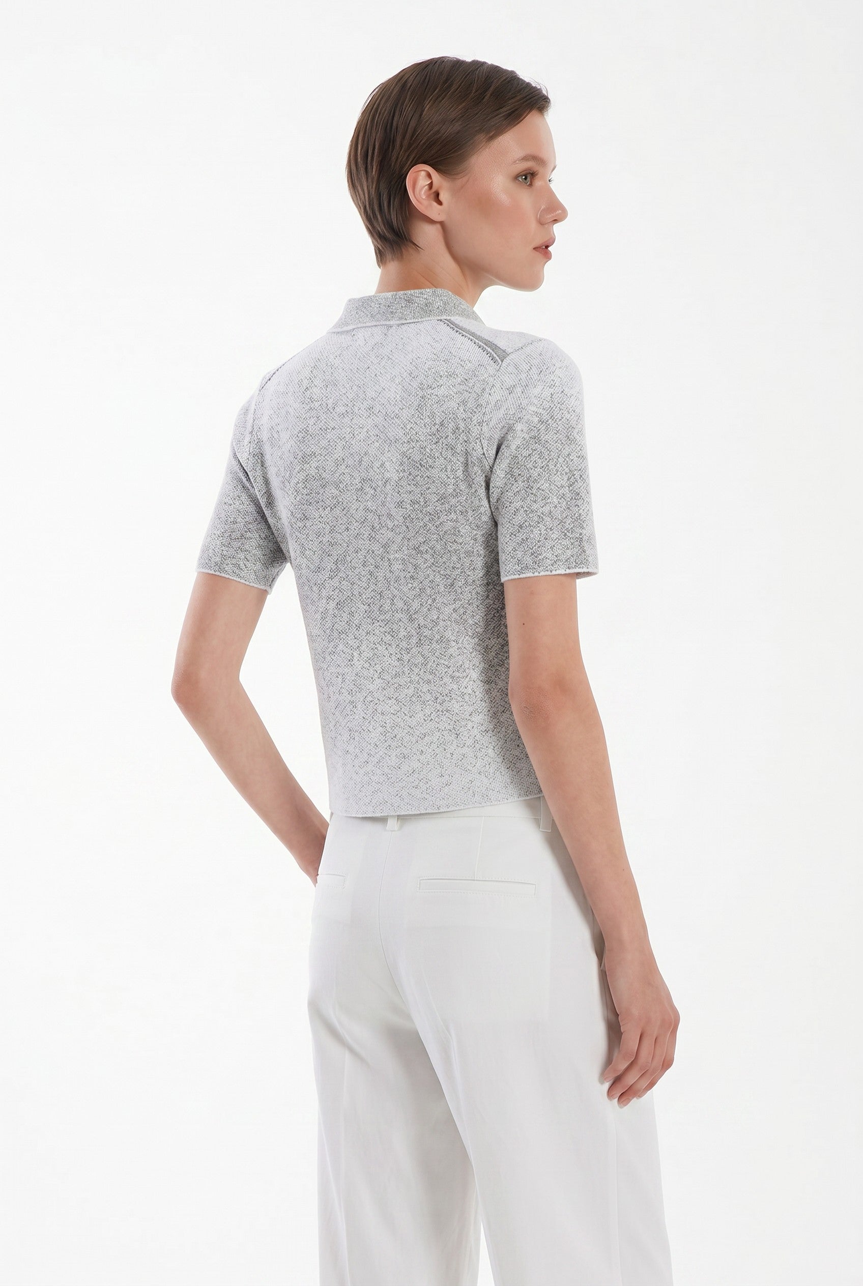 The back of a woman wearing a gray polo shirt and white pants on a white background.