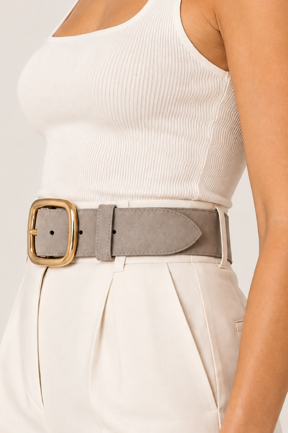 A side view close-up of a model wearing a wide taupe-brown belt with a gold-tone rectangular buckle, styled over a white ribbed tank top and cream trousers.