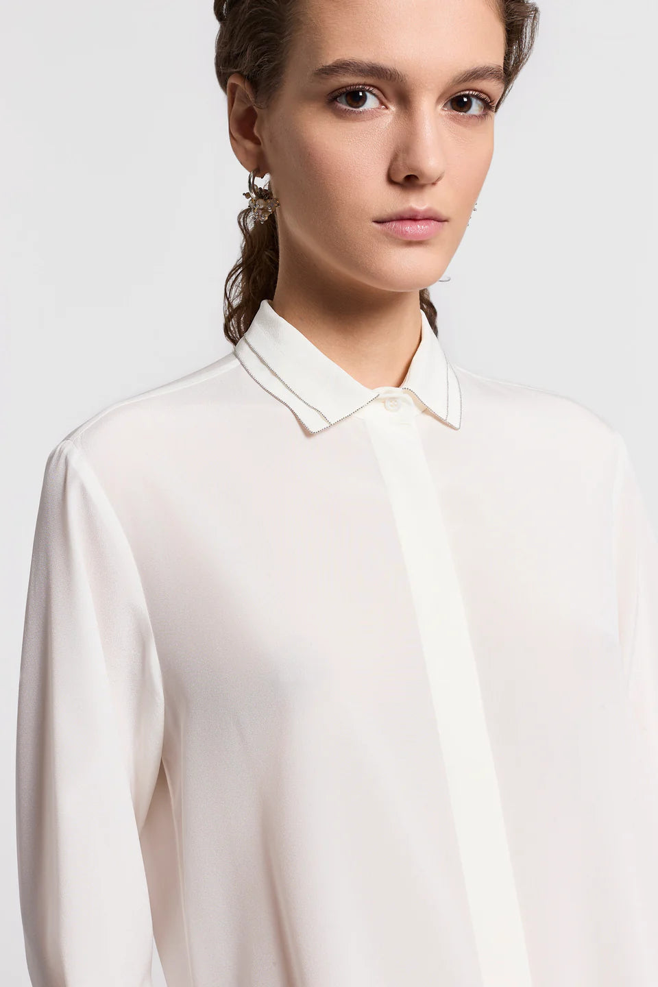 Close-up of a woman wearing a white blouse with sparkle detailing, against a light gray background.