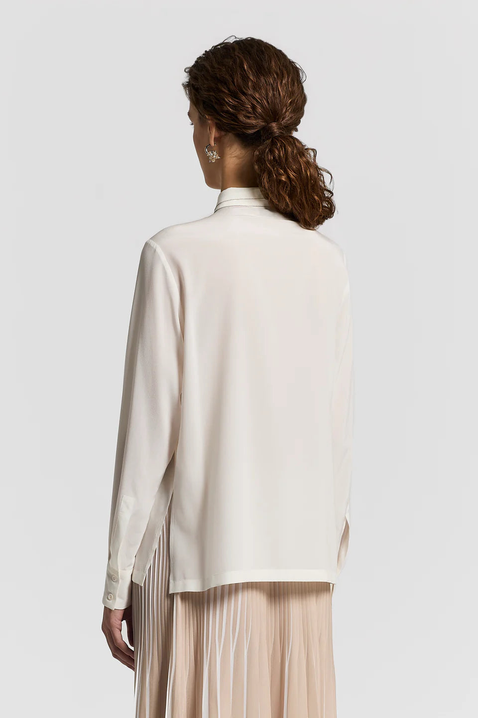 The back of a woman wearing a white blouse with a plain background.