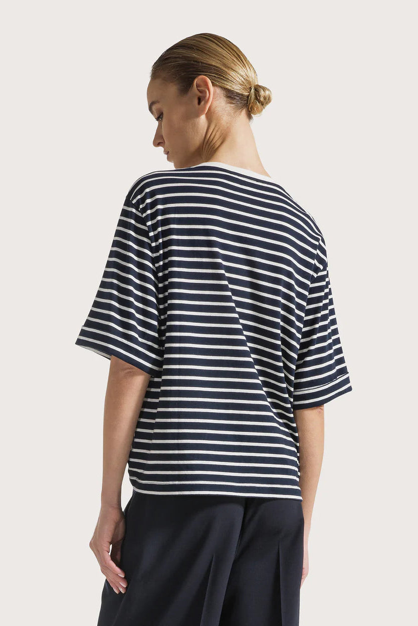 Back of a woman wearing a navy and white striped shirt on a plain background.