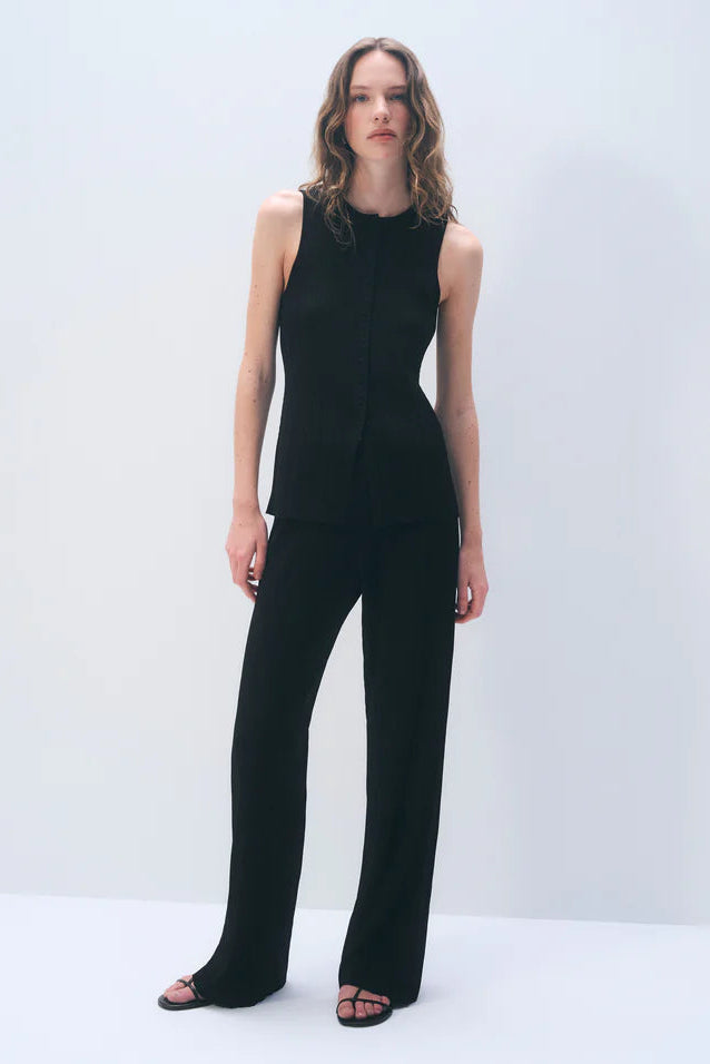 Woman wearing a black vest top with matching pants against a white background.