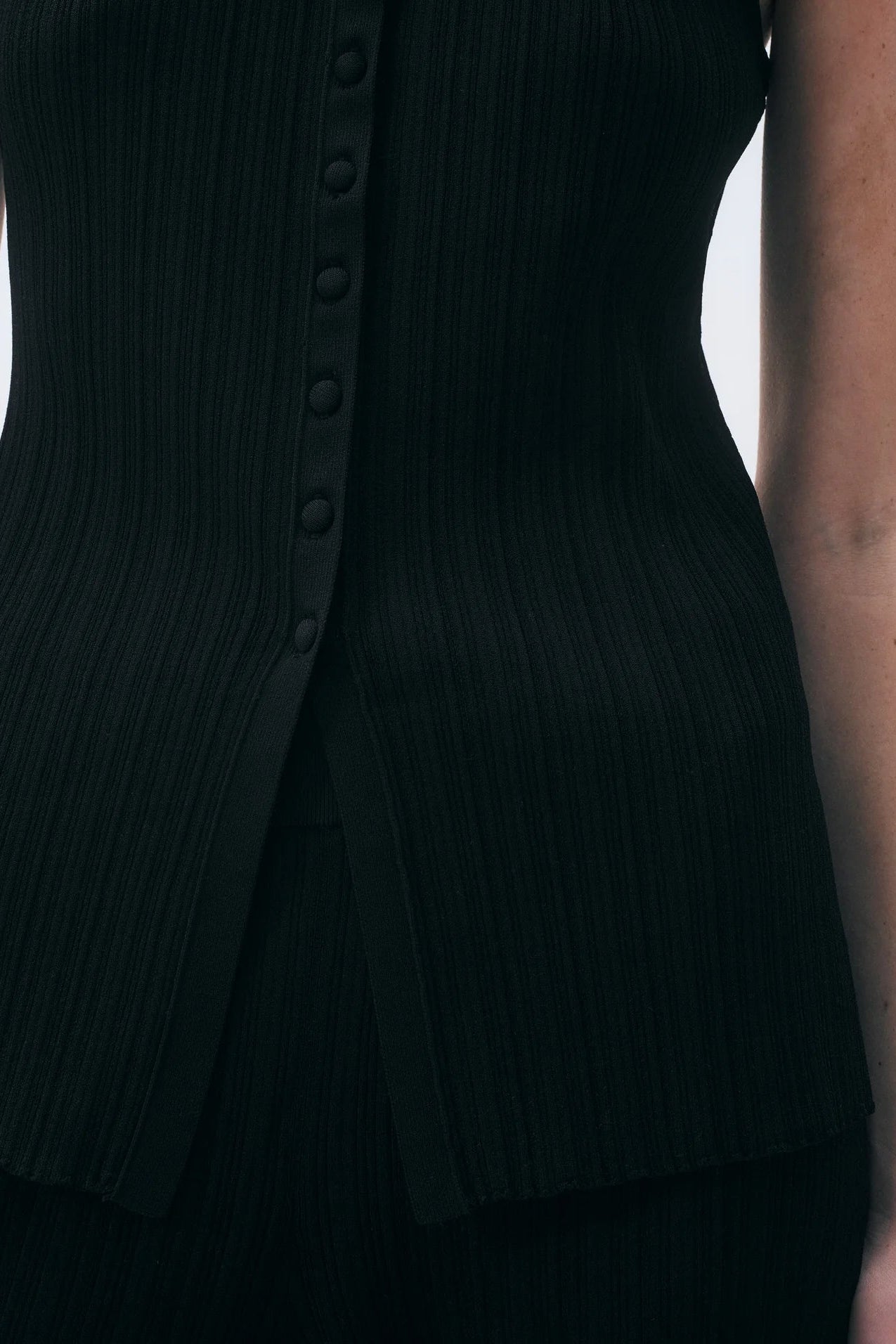 Close up of a black vest top with button details on a plain background.