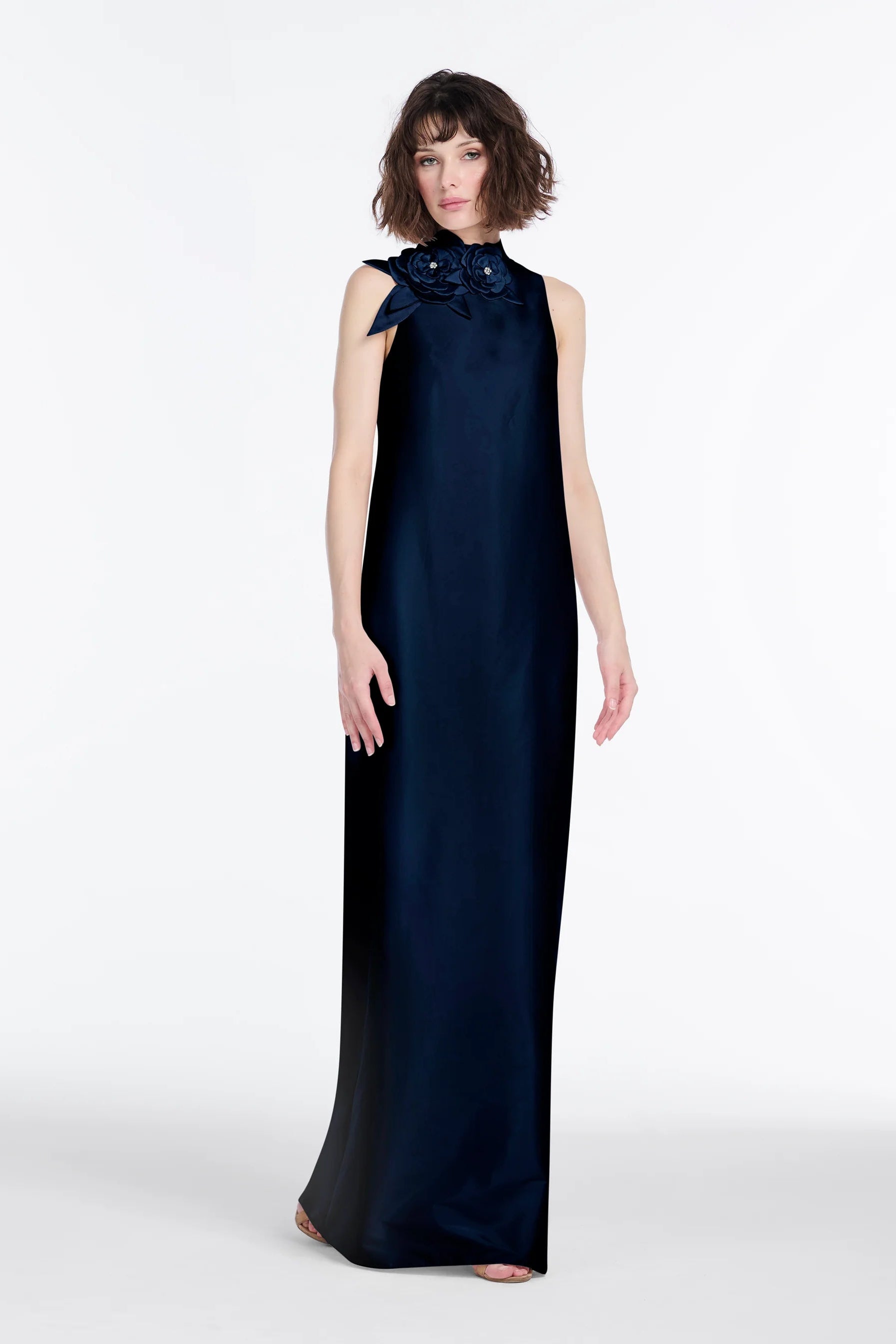 Woman wearing a navy blue evening gown with a floral detail on a white background.