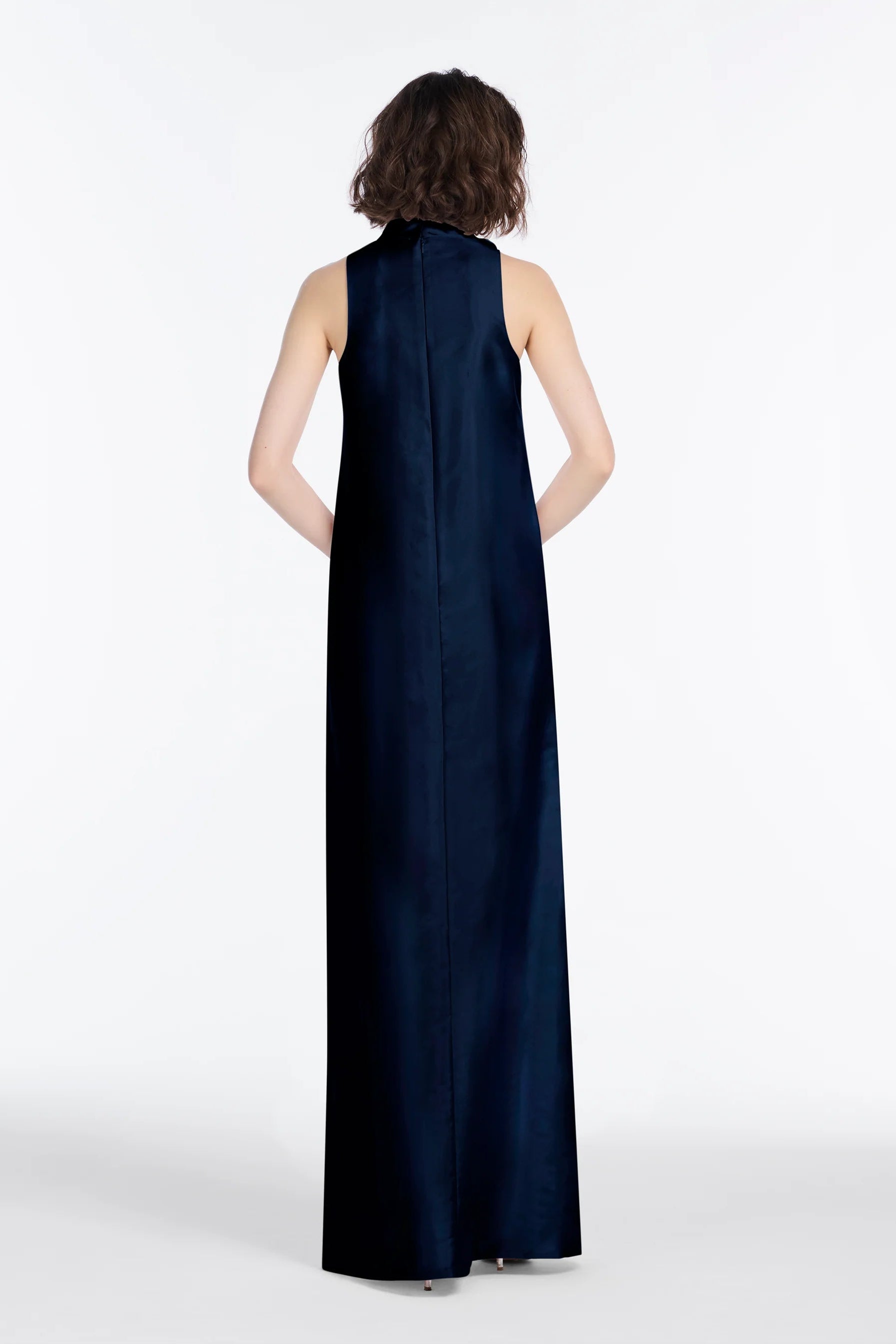 The back of a woman wearing a long navy dress on a white background.