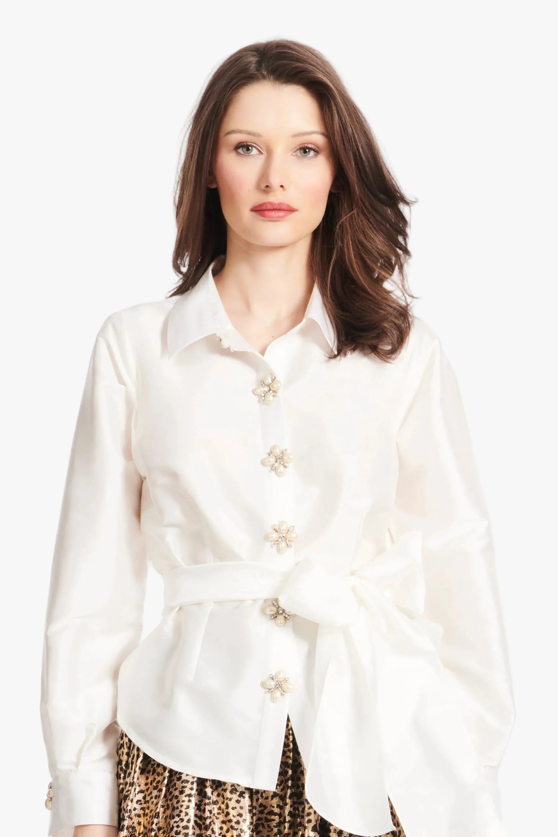 Woman wearing a white blouse with floral buttons on a plain background.
