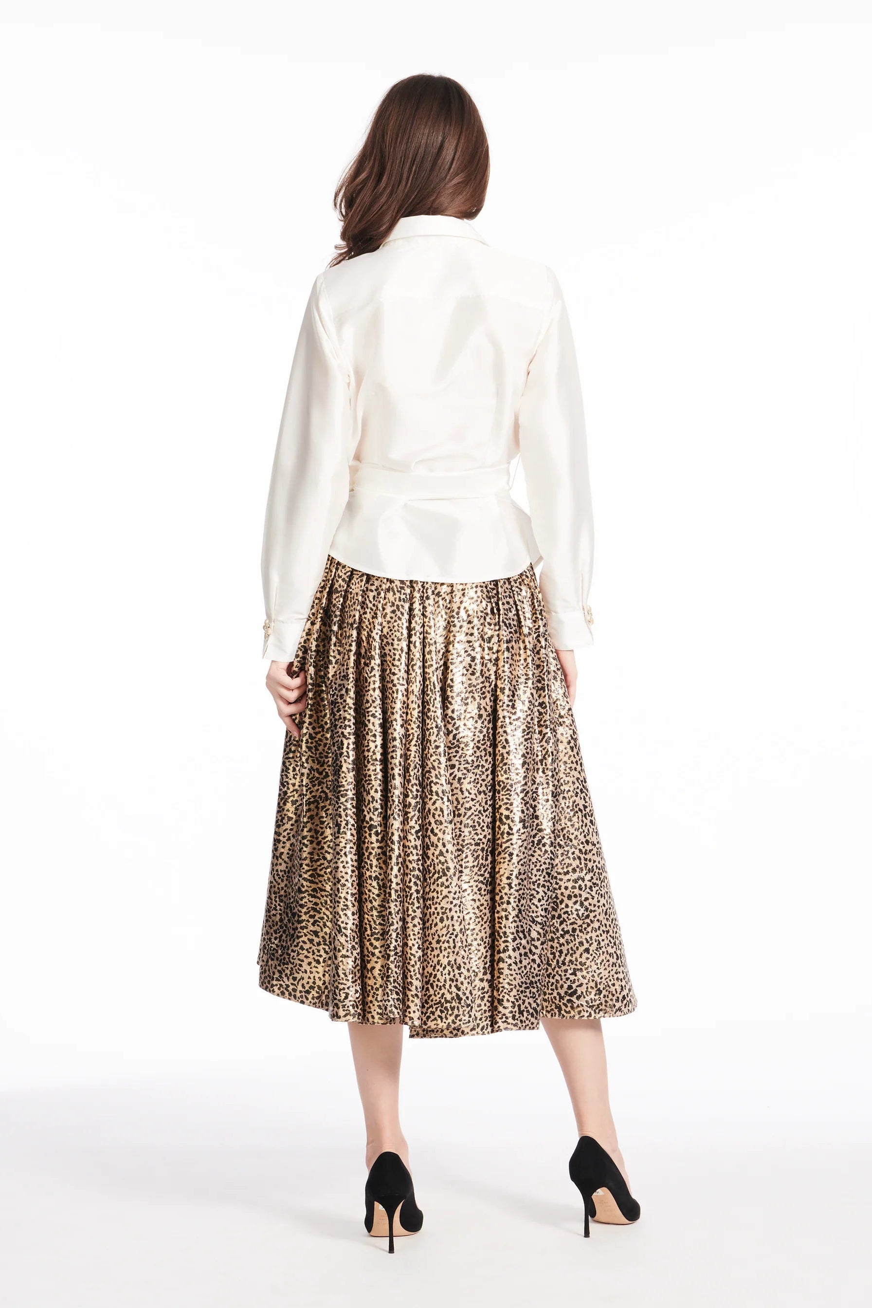The back of a woman wearing a white blouse and leopard print skirt on a white background.