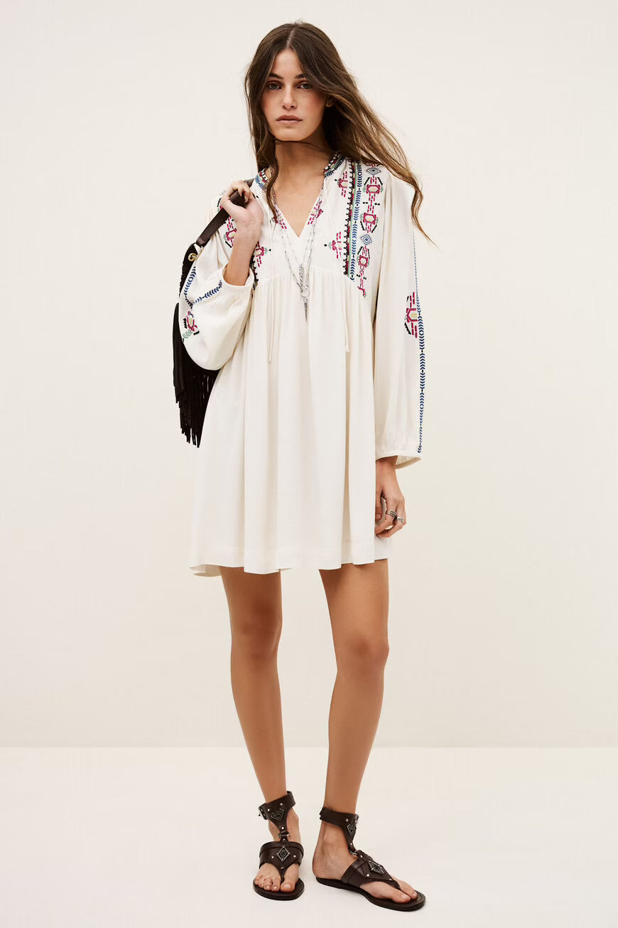 Woman wearing a white dress with colorful embroidery on a plain background.