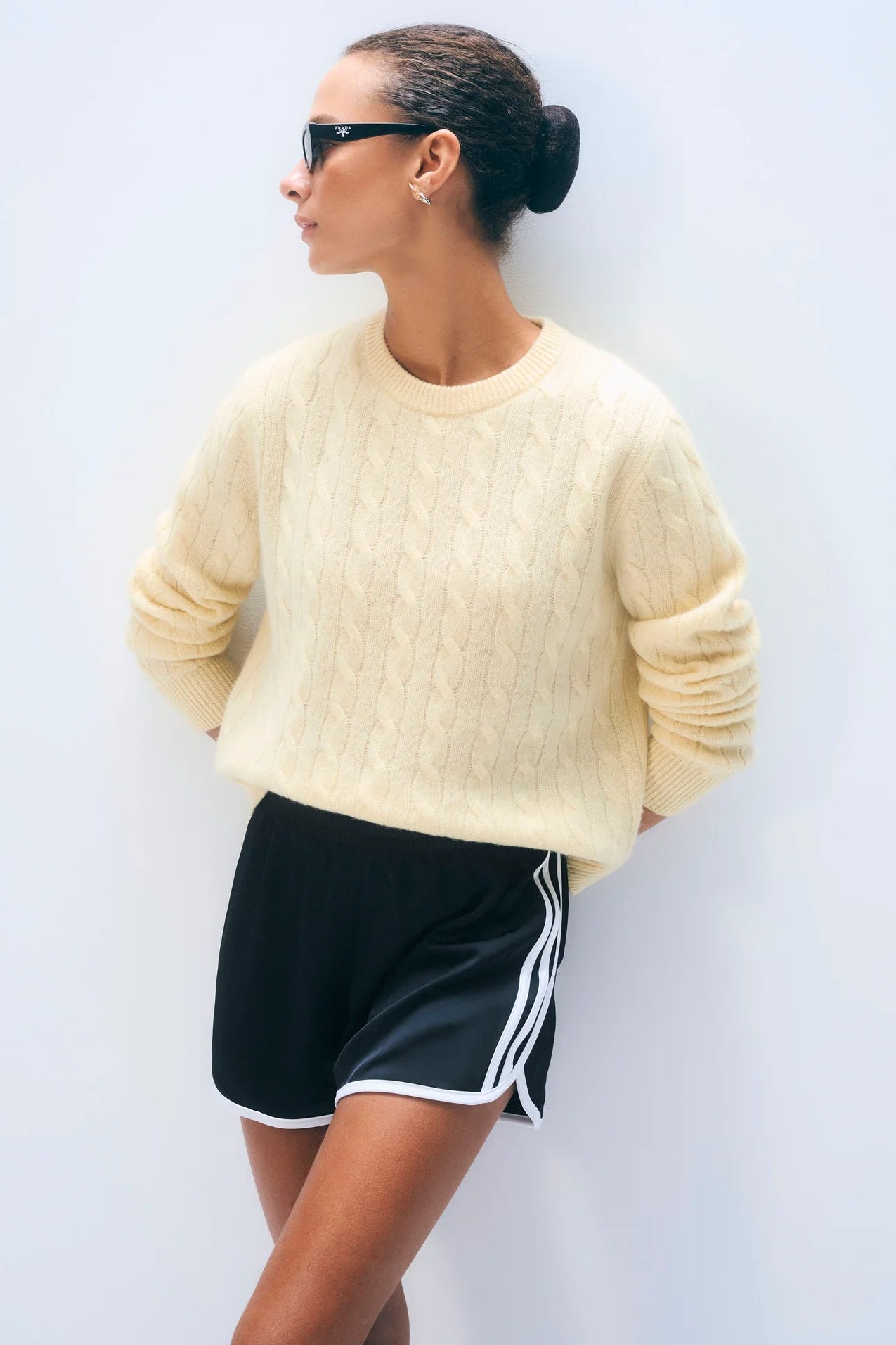 Person wearing a light yellow sweater and black shorts with white stripes on a plain background.