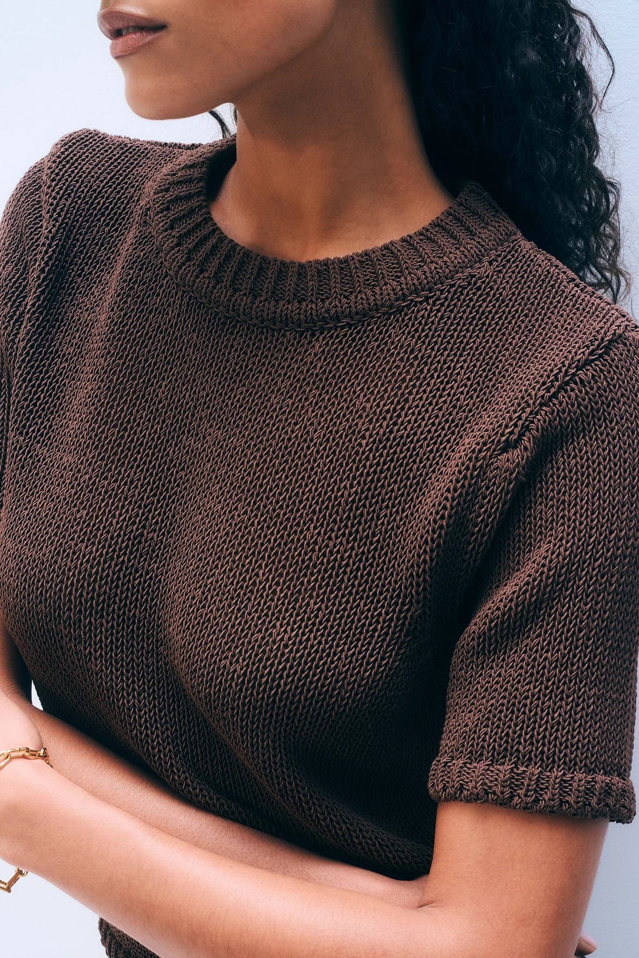 Close-up of woman wearing a brown short sleeve sweater against a light background.