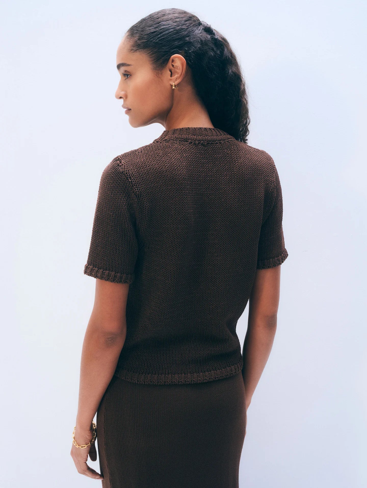 The back of a woman wearing a brown short-sleeve top against a light blue background.