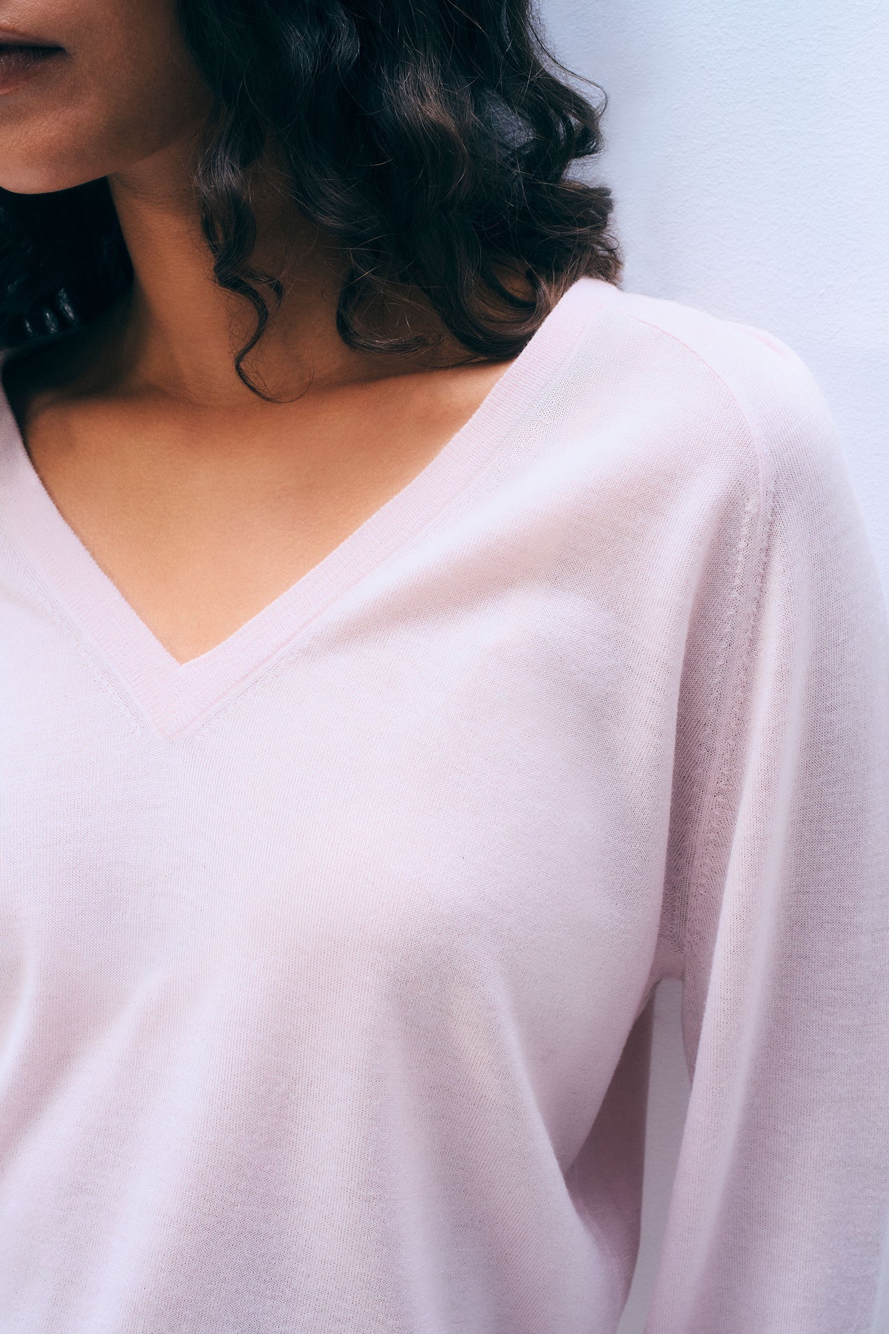 Close-up of a woman wearing a light pink sweater with a blurred background.