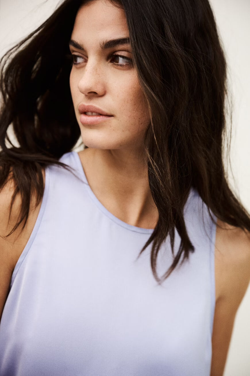 Close-up of a woman wearing a light purple sleeveless top with a neutral background.