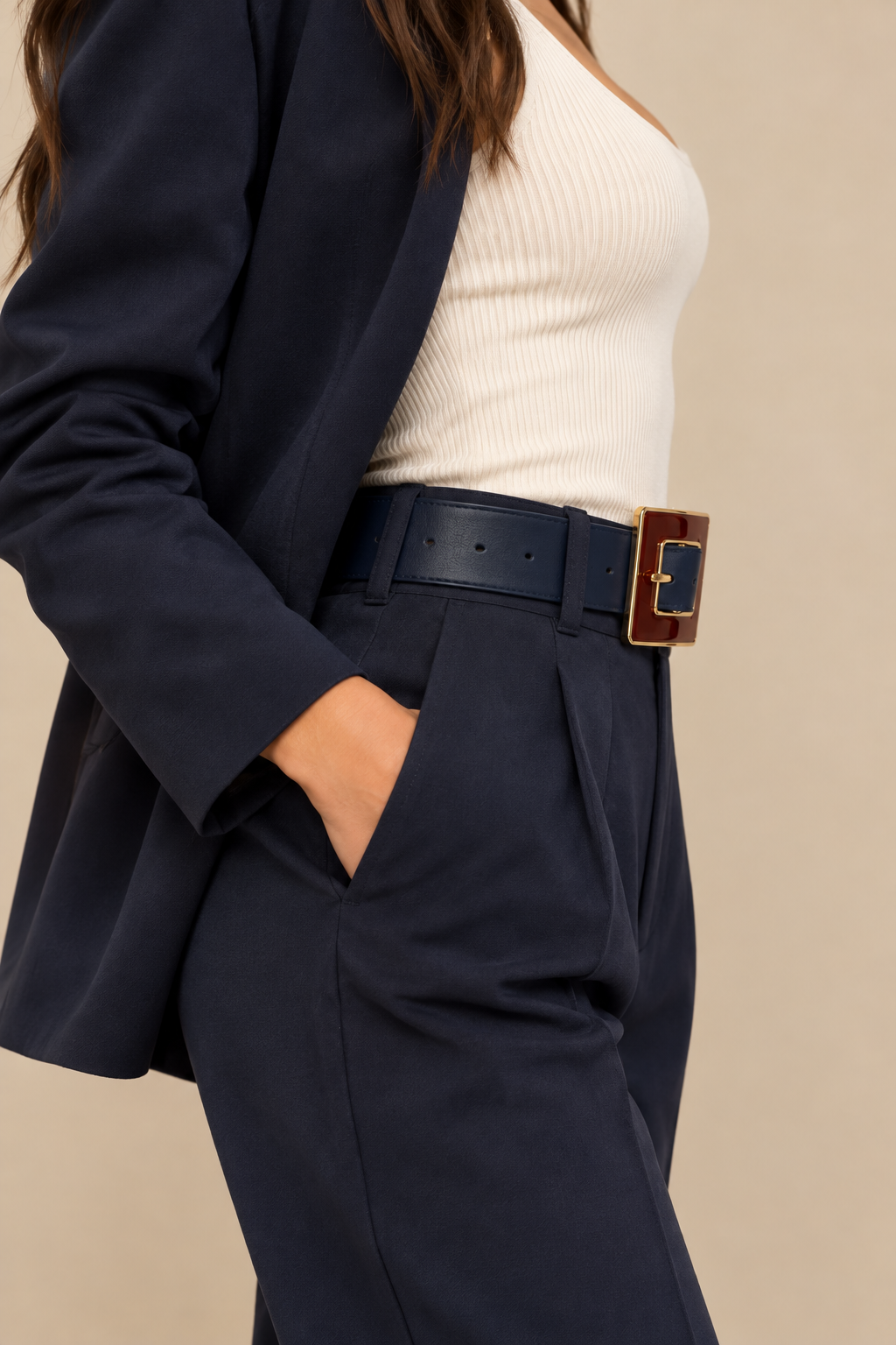 Side view of the Gavazzeni Angelica navy blue leather belt with a burgundy and gold-tone statement buckle, styled through the belt loops of navy tailored trousers with a matching blazer and ivory ribbed top.