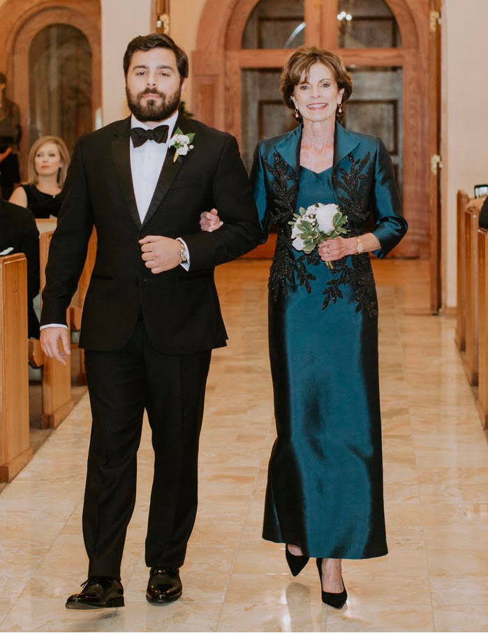 Man in a tuxedo and woman in a joseph plato teal dress walking down a hallway with a chandelier.