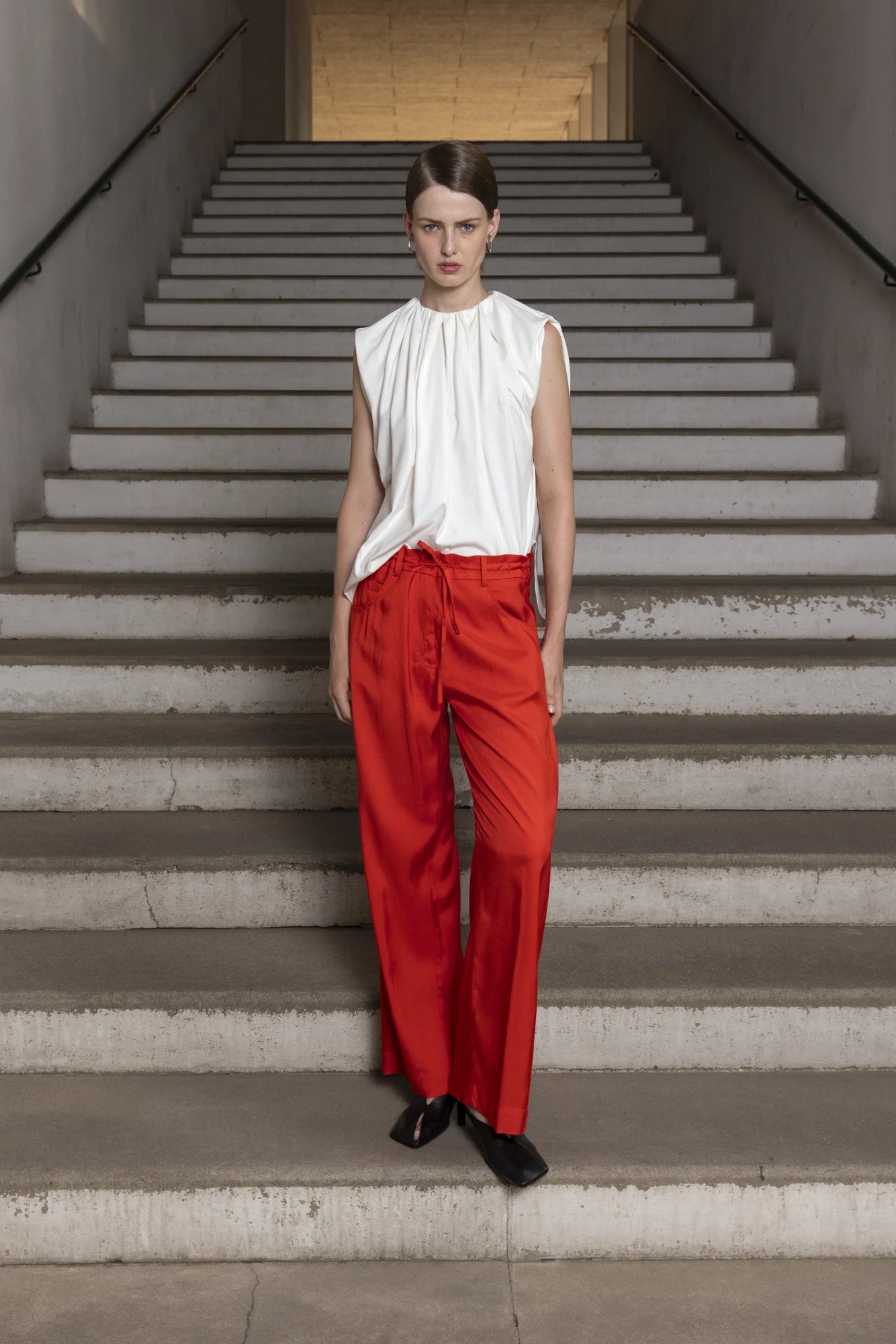 Woman in a white top and red pants standing on concrete stairs.