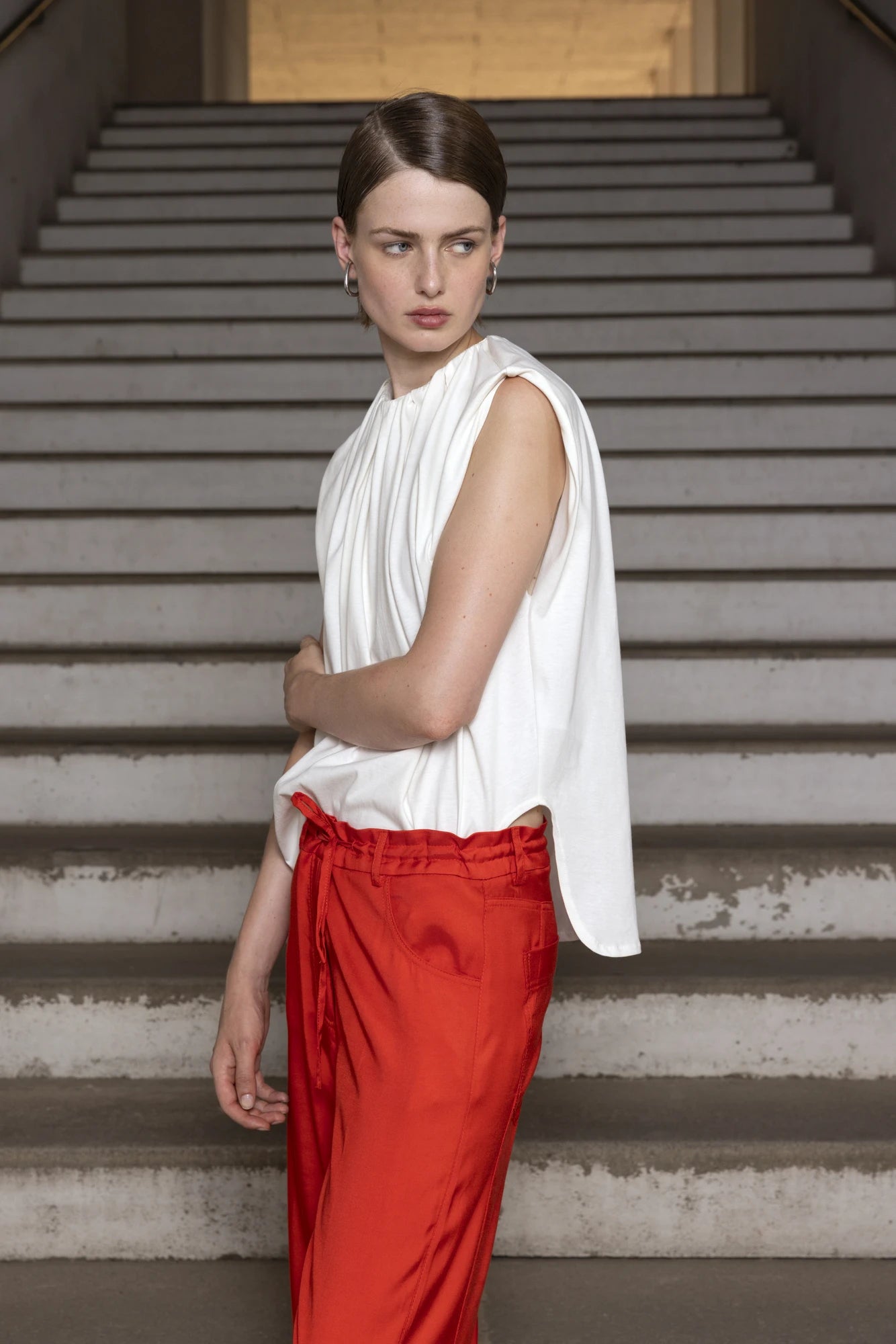 Woman in a white sleeveless top and red pants standing on stairs.