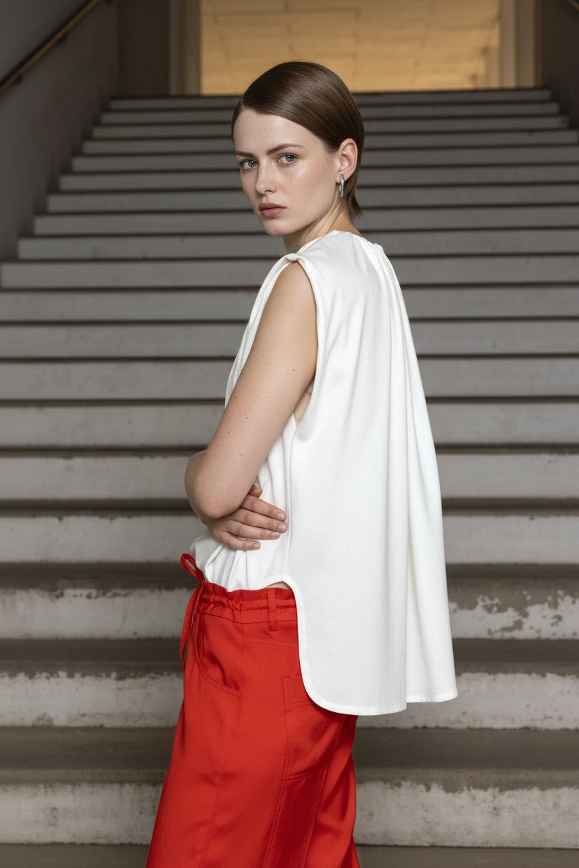 Woman in a white sleeveless top and red pants standing on steps.