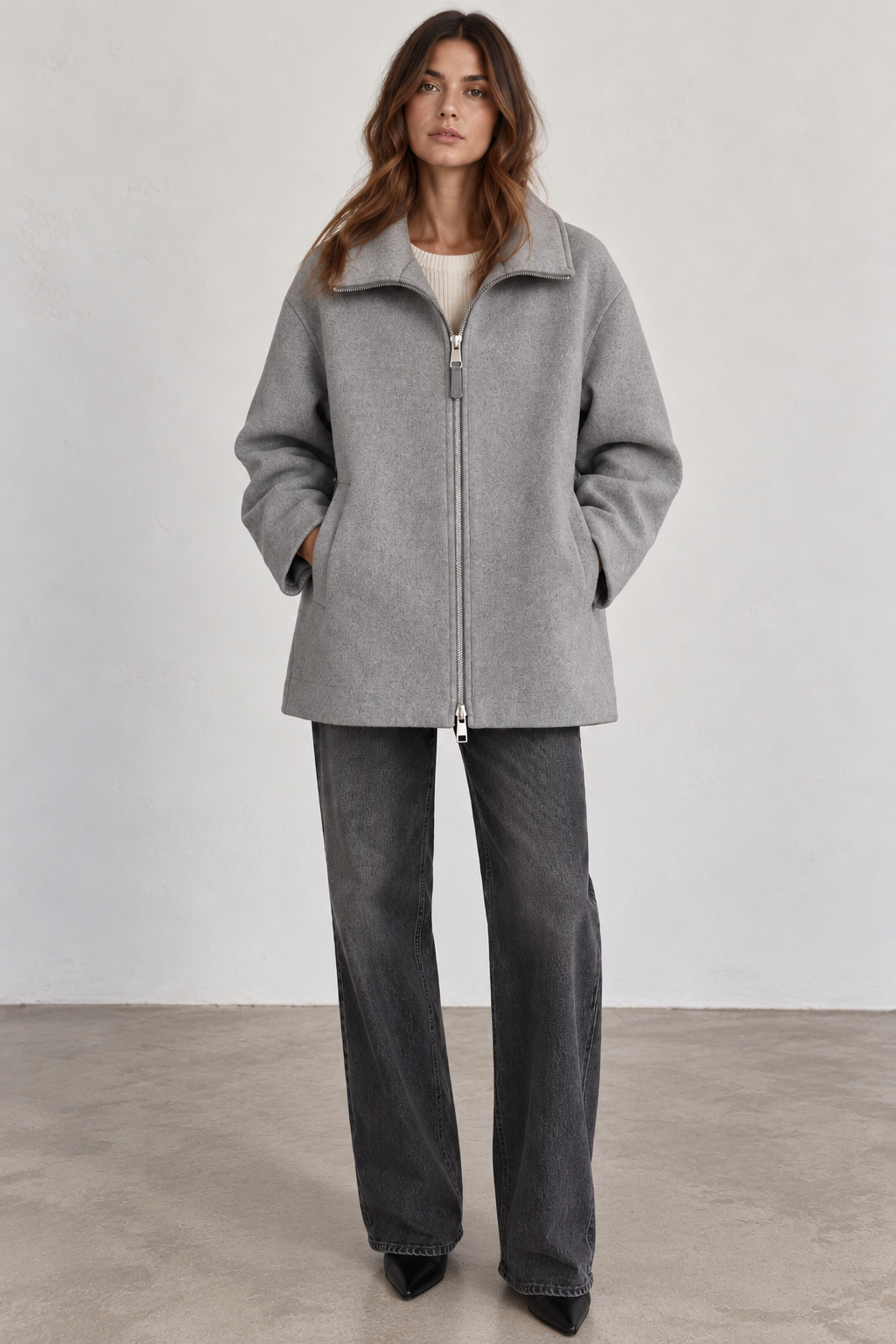Front view of model wearing a Seventy gray wool-blend coat without the removable padded collar, featuring a relaxed, boxy silhouette, structured stand collar, silver two-way front zipper, long sleeves, and side pockets, styled with charcoal wide-leg jeans and black pointed-toe boots.